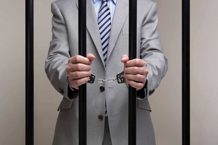 136074335 featured image Person in suit handcuffed behind jail bars.