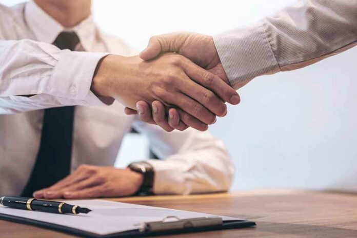 708556399 featured image Two people shaking hands over a desk.