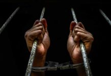 Hands in handcuffs gripping jail bars.