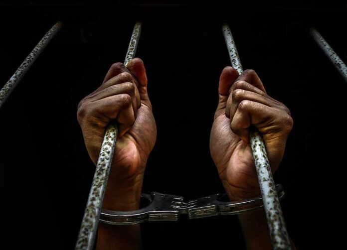 550272775 featured image Hands in handcuffs gripping jail bars.