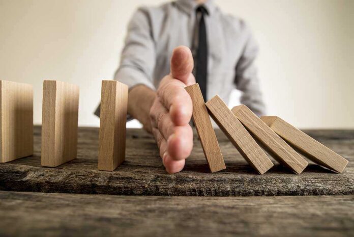560750821 featured image Hand stops falling dominoes on wooden table