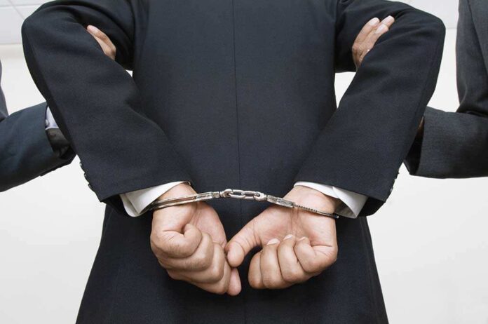 121141399 featured image Person handcuffed in suit escorted by two others