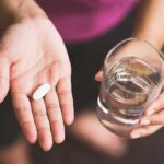 Hand holding pill and glass of water