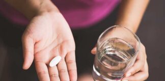 Hand holding pill and glass of water