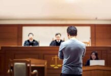 Man stands in courtroom before judges and stenographer