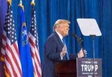 Person speaking at podium with flags in background
