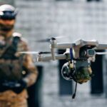 Military personnel operating drone with mounted device