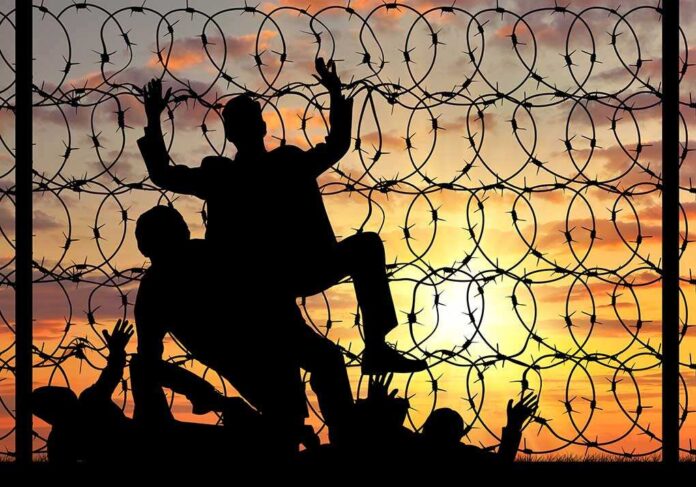 Silhouettes of people climbing barbed wire fence