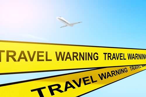 TRAVEL ADVISORY WARNING_2086996915 featured image Yellow travel warning tape with airplane in sky