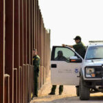 Border patrol agents near a tall metal fence