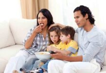 A family of four enjoying a movie night on the couch with snacks