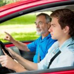 A young man driving a car with an older man giving instructions