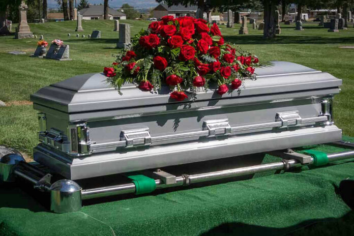 Silver casket with rose bouquet in a cemetery.