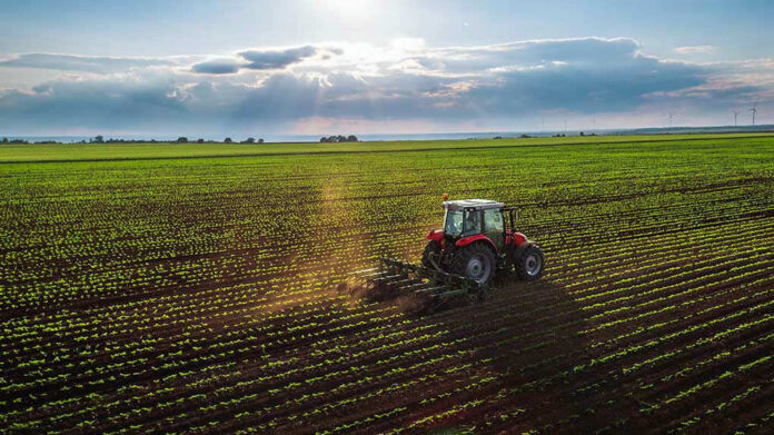Tractor plowing a vast green field at sunset.