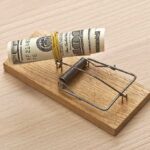 A rolled stack of cash secured in a mousetrap on a wooden surface