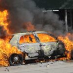 A car engulfed in flames with thick smoke billowing into the air
