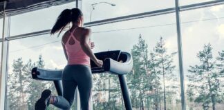 A woman running on a treadmill in a gym with large windows