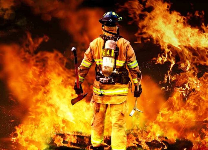 Firefighter standing in front of a large fire, equipped with tools
