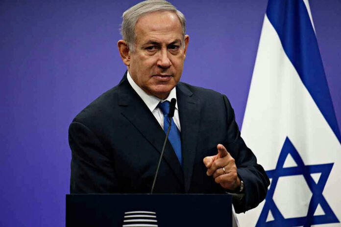 Man in suit giving speech in front of Israeli flag.