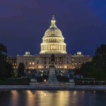 Illuminated capitol building at night with reflection in water.