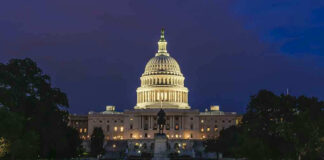 Illuminated capitol building at night with reflection in water.