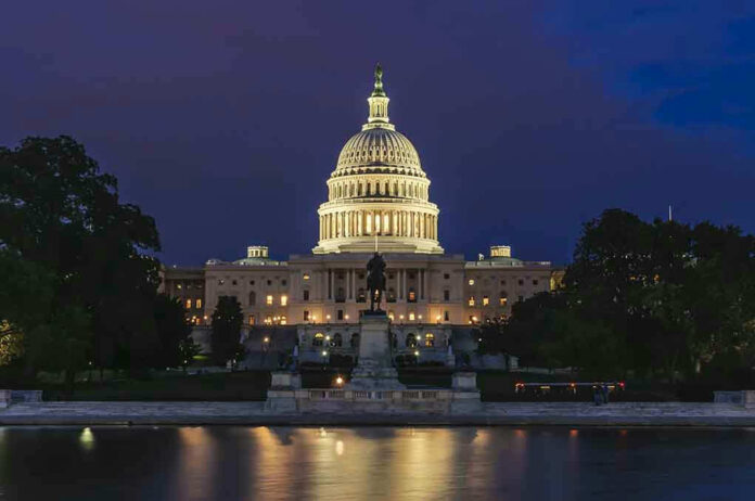 Illuminated capitol building at night with reflection in water.