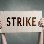 Two hands holding a cardboard sign saying STRIKE.