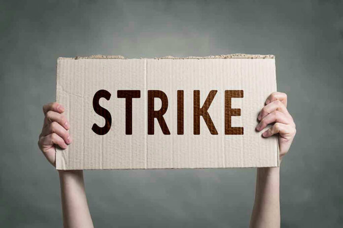 Two hands holding a cardboard sign saying STRIKE.