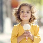 A young child with curly hair holding an ice cream cone outdoors