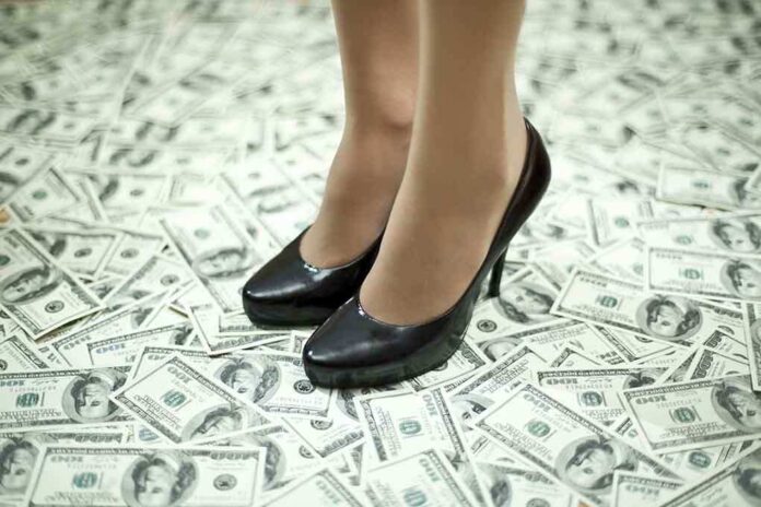 A pair of black high heels standing on a floor covered with dollar bills