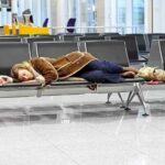 A traveler sleeping on a bench in an airport waiting area