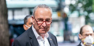 Man in suit and red glasses standing outside.