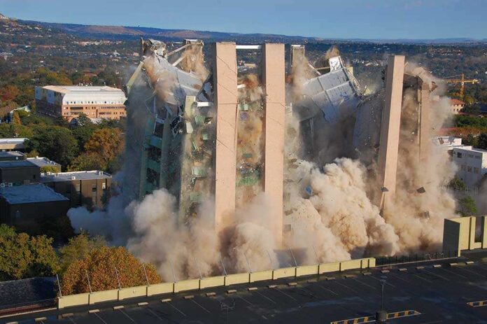 A building being demolished with dust and debris in the air