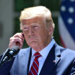 Trump Blocks Refugees – Except for ONE NATION Man in a suit adjusting an earpiece.
