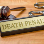 Gavel, handcuffs, and Death Penalty sign on desk.