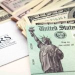 A tax refund check from the IRS alongside various denominations of cash