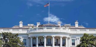 The White House with the American flag flying against a blue sky