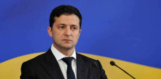 Man in suit speaking at podium with microphones.