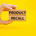 Hand holding Product Recall blocks on yellow background.
