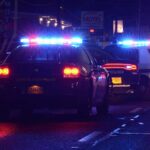 Police cars with flashing lights at a nighttime scene near a motel