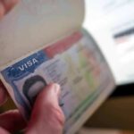 A hand holding an open passport displaying a visa page