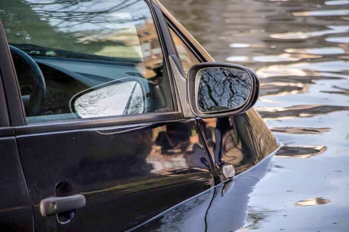 A partially submerged black car in floodwaters
