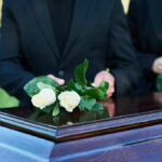 People placing white roses on a casket.