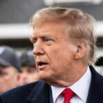 Man in suit and red tie speaking outside.