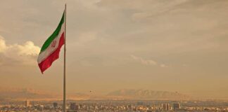 Iranian flag waving over a city skyline with mountains in the background