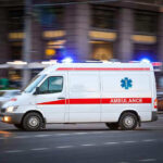Ambulance driving on urban street with lights flashing.