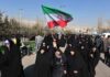 Group of women in black attire marching with an Iranian flag
