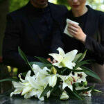 Mourners in black holding white flowers at funeral.