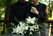 Mourners in black holding white flowers at funeral.
