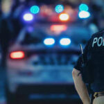 Police officer with patrol car and flashing lights.